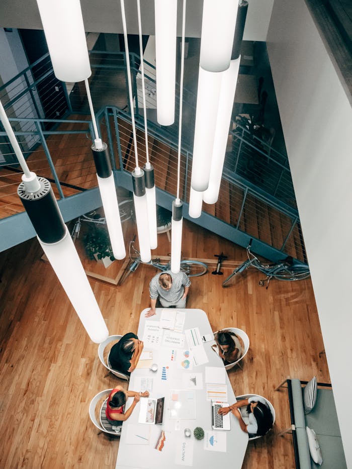 pexels-photo-7688333 High angle shot of team collaborating at a stylish desk with ceiling lights in a modern office.